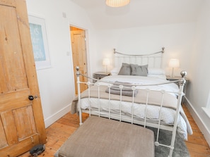Une chambre à coucher avec un lit en métal blanc, deux tables de chevet avec des lampes, une porte en bois et un petit tapis.