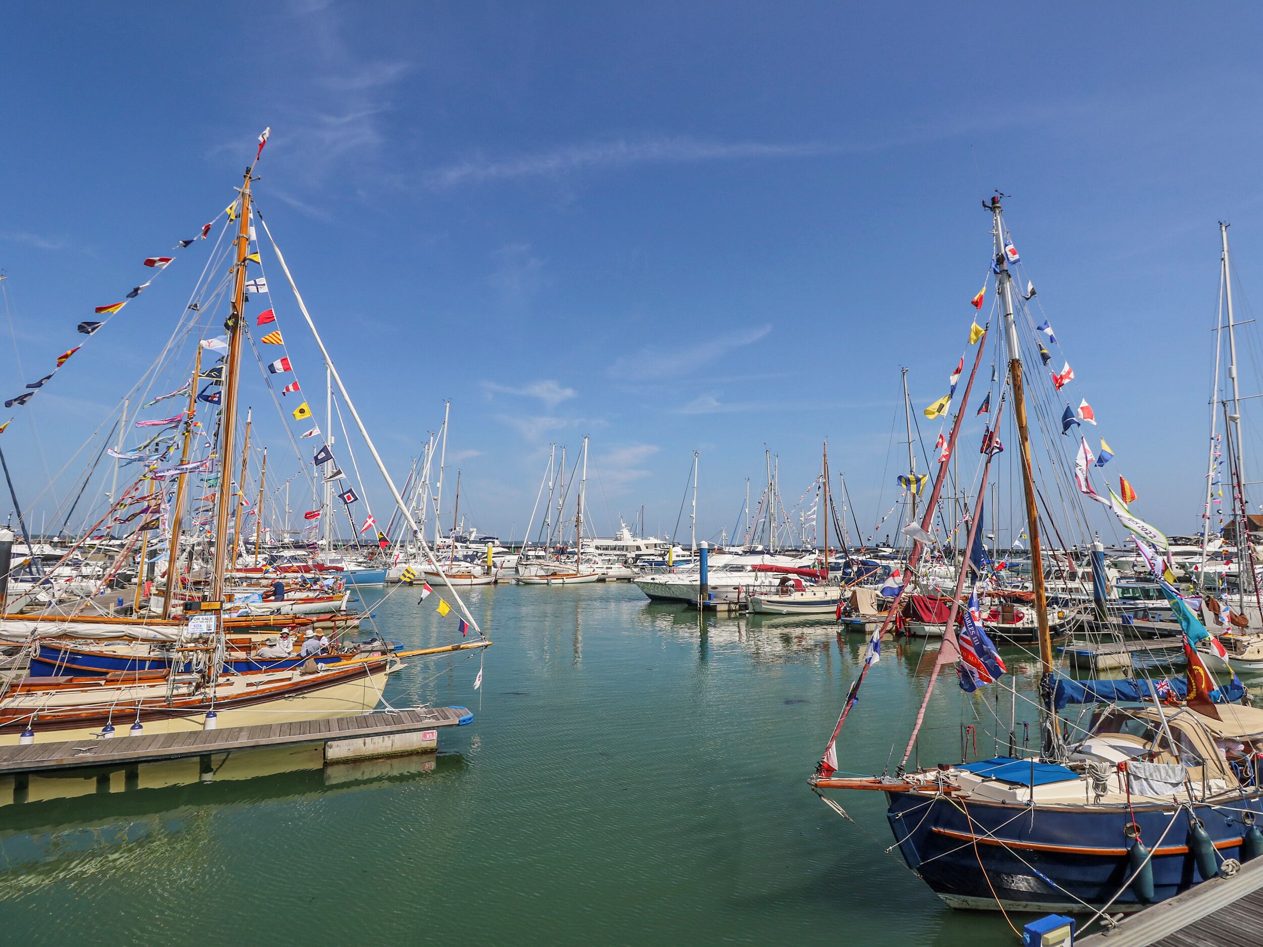 Un port de plaisance où de nombreux bateaux sont amarrés, le ciel est dégagé et l’eau est calme.
