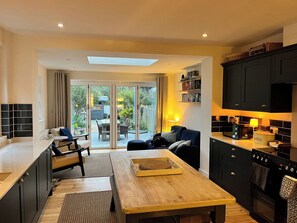 A modern kitchen with dark cabinets, a wooden dining table, and a view of the outdoor patio. - 4 Copse Lane (Freshwater)