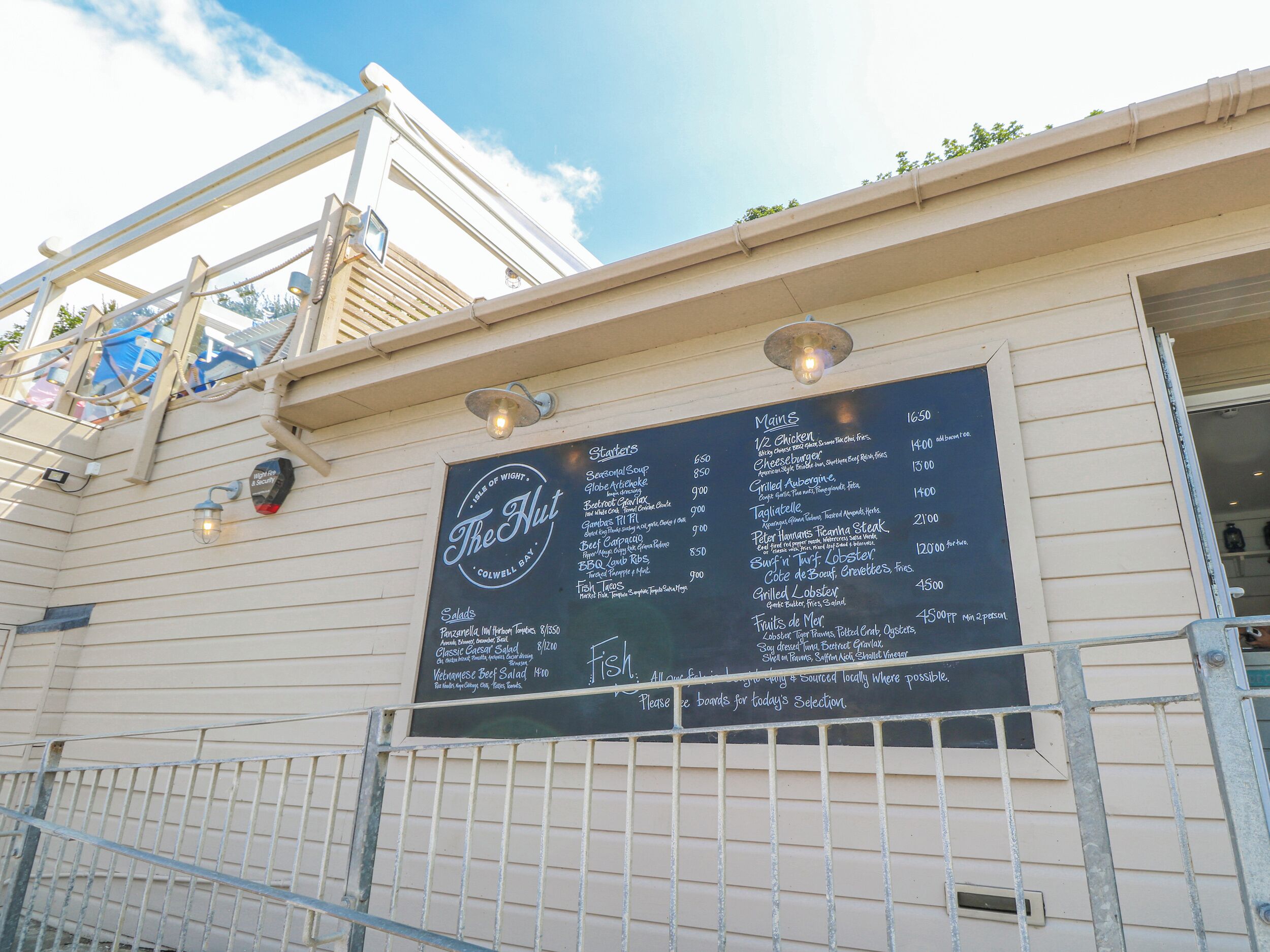 A menu board for 'The Hut' restaurant with a list of mains, salads, and fish options.