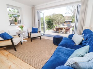 A modern living room with a sofa, chairs, a small table, and a view of the outdoors. - 4 Copse Lane (Freshwater)