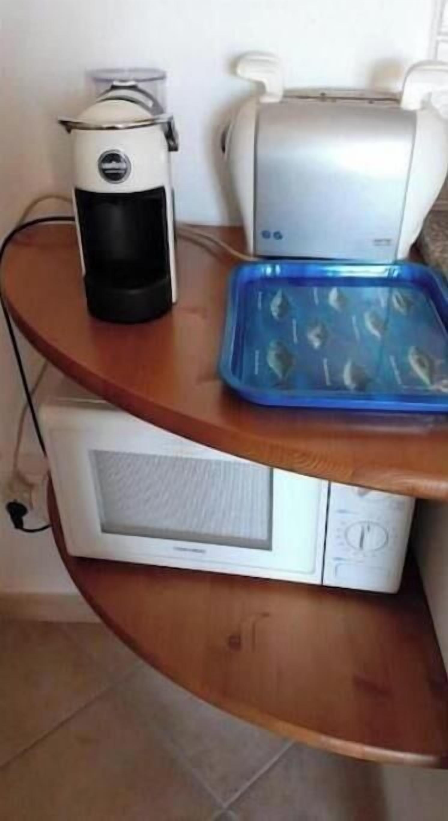 Una encimera de cocina con una cafetera, un tostador y una bandeja azul con alimentos.
