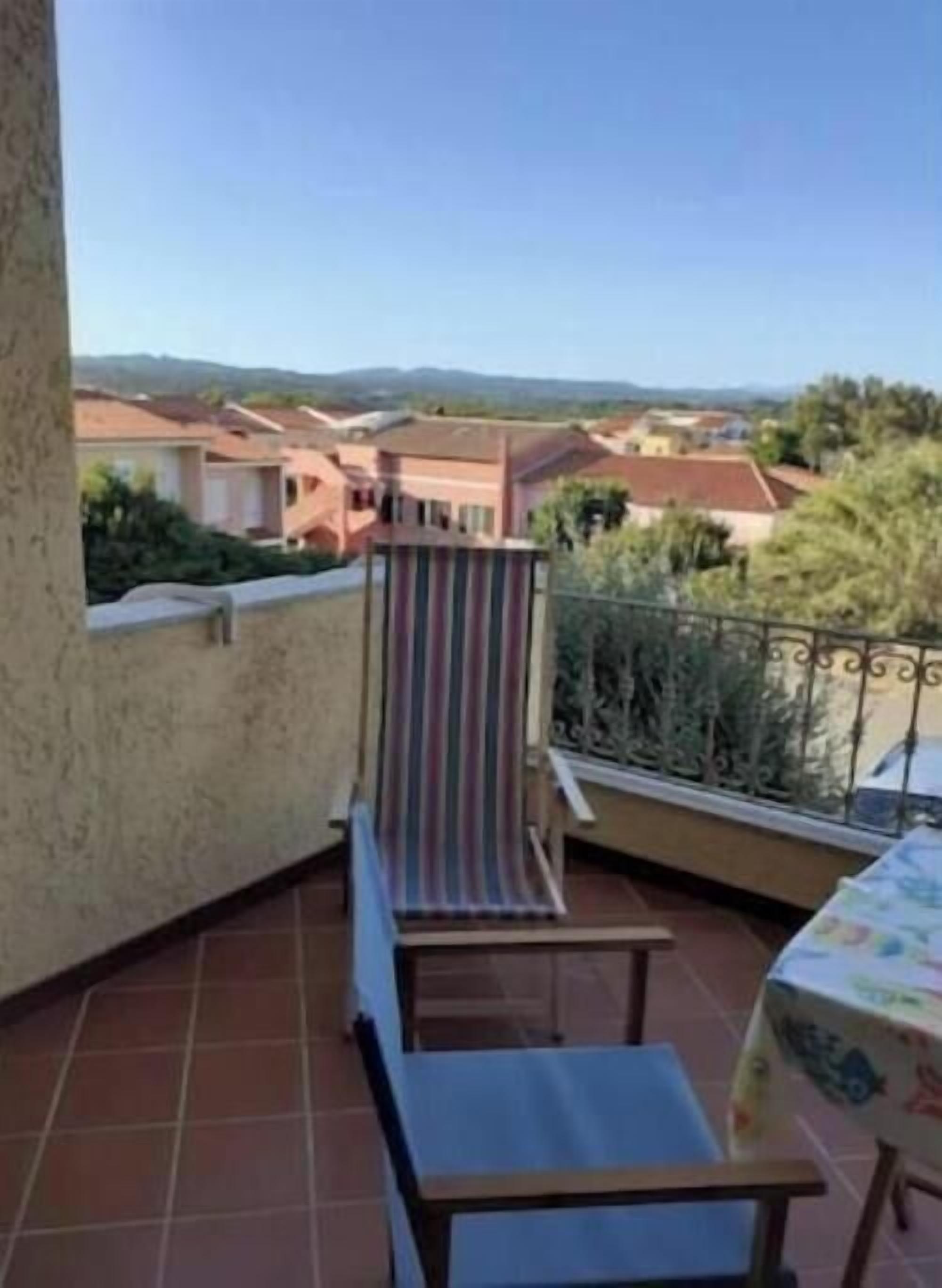 Ein Balkon mit einem gestreiften Stuhl, einem kleinen Tisch und Blick auf Häuser in der Ferne.