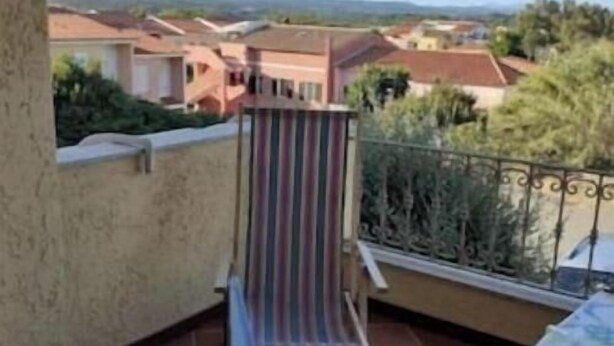 Un balcón con una silla a rayas, una mesita y vistas a casas en la distancia.