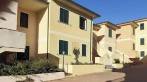 Una hilera de edificios color beige con balcones, un sendero pavimentado y algo de vegetación.
