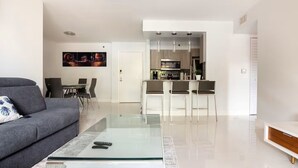 Ein modernes Wohnzimmer mit einem Glastisch, einem grauen Sofa und einem Essbereich mit Stühlen.
