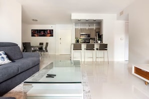 Ein modernes Wohnzimmer mit einem Glastisch, einem grauen Sofa und einem Essbereich mit Stühlen.