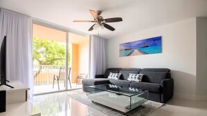 Ein modernes Wohnzimmer mit einer Couch, einem Glastisch, einem Deckenventilator und einem Bild an der Wand.