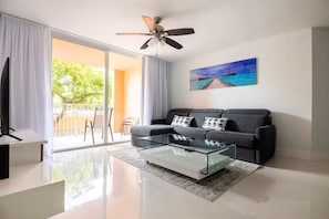 Ein modernes Wohnzimmer mit einer Couch, einem Glastisch, einem Deckenventilator und einem Bild an der Wand.