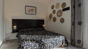 A bedroom with a bed, bedside lamps, a framed picture, and decorative wall hangings. - Air-conditioned studio for 2 people, near the shops (Grasse)