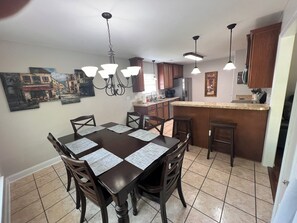 A dining area with a dark wooden table and chairs, a kitchen with wooden cabinets and a granite countertop, and a ceiling fan.