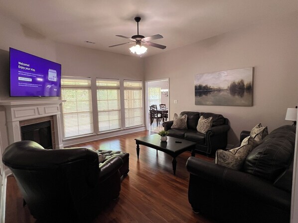 A living room with a fireplace, a ceiling fan, a television, and a painting on the wall.