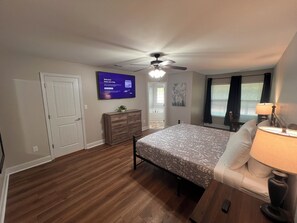 A bedroom with a bed, a dresser, a ceiling fan, a TV, and a window with blinds.