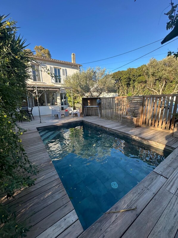 A backyard with a swimming pool, wooden deck, and a fenced area.
