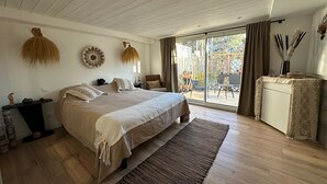 Ein Schlafzimmer mit einem großen Bett, Holzboden, einem kleinen Tisch und Blick ins Freie.