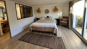 Ein Schlafzimmer mit einem großen Bett, einem Nachttisch, einem Spiegel und Blick ins Freie.