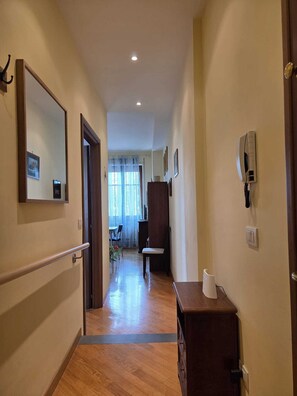Un pasillo con suelo de madera, un banco de madera, un teléfono en la pared y un espejo.