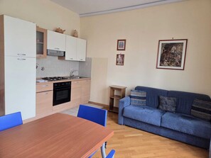 Una cocina compacta con una mesa de comedor y un sofá, un estante pequeño y dos cuadros en la pared.