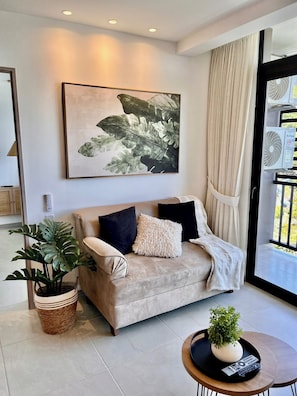 Un salon moderne avec un canapé beige, un grand tableau abstrait, une plante en pot et une petite table ronde sur laquelle se trouve une télécommande.