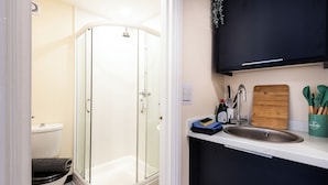 Et moderne badeværelse med et glasvægshus, toilet og et vaskebord med skærebræt og køkkenredskaber.
