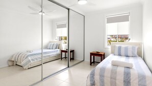 Un dormitorio con armario de espejo, dos camas, una mesita pequeña y ventana con vistas.