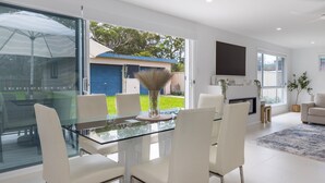 Un comedor moderno con una mesa de vidrio, sillas blancas y un jarrón con plantas secas.