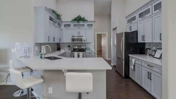 Une cuisine moderne avec des meubles blancs, un îlot central, des appareils en acier inoxydable et un tabouret de bar.