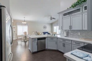 A modern kitchen with grey cabinets, a dishwasher, and a dining area with a table and chairs. - Heated Pool Chandler Home & Chef's Kitchen! (Chandler)