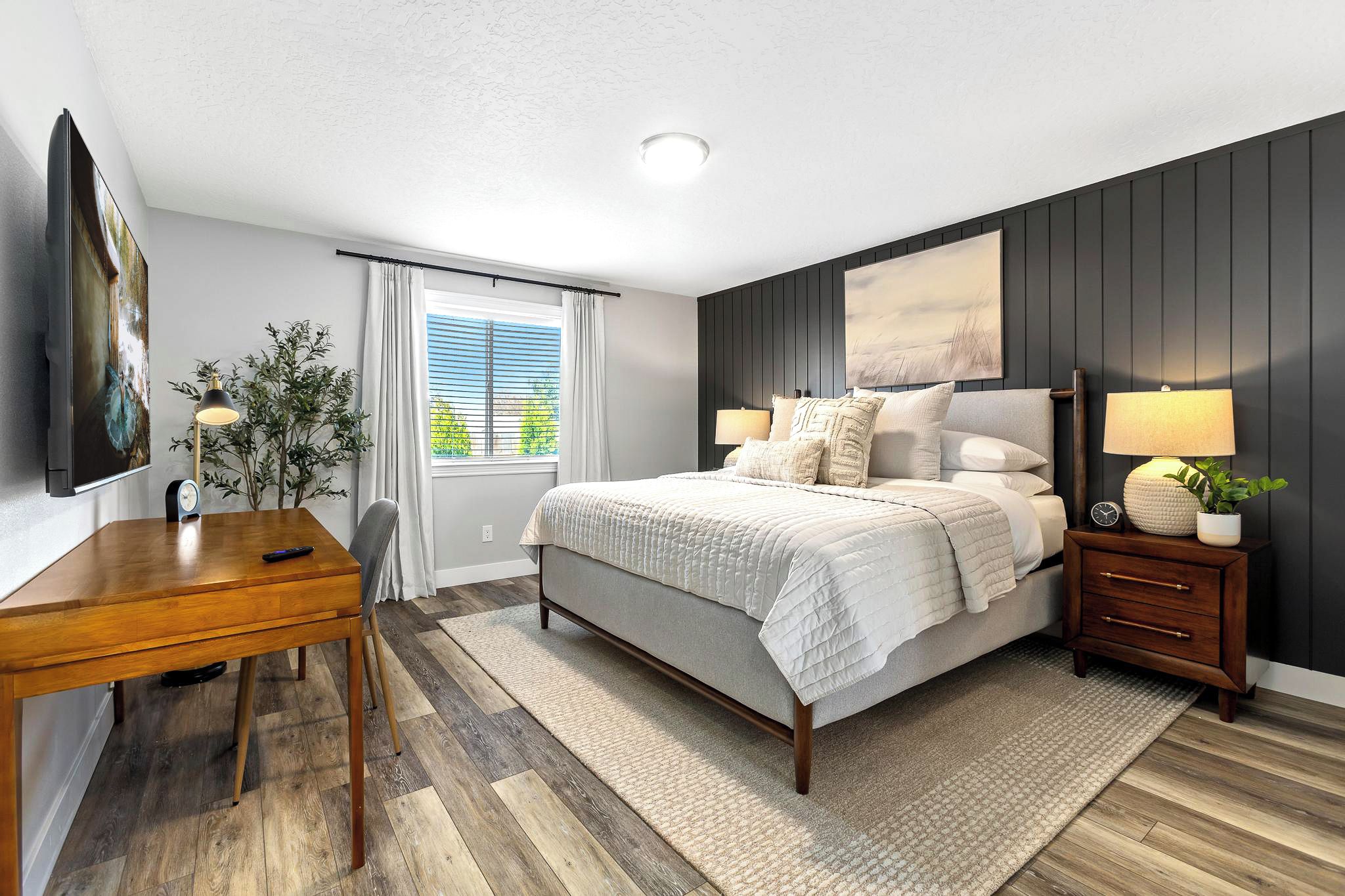 A bedroom with a bed, bedside tables, a desk, and a window with curtains.