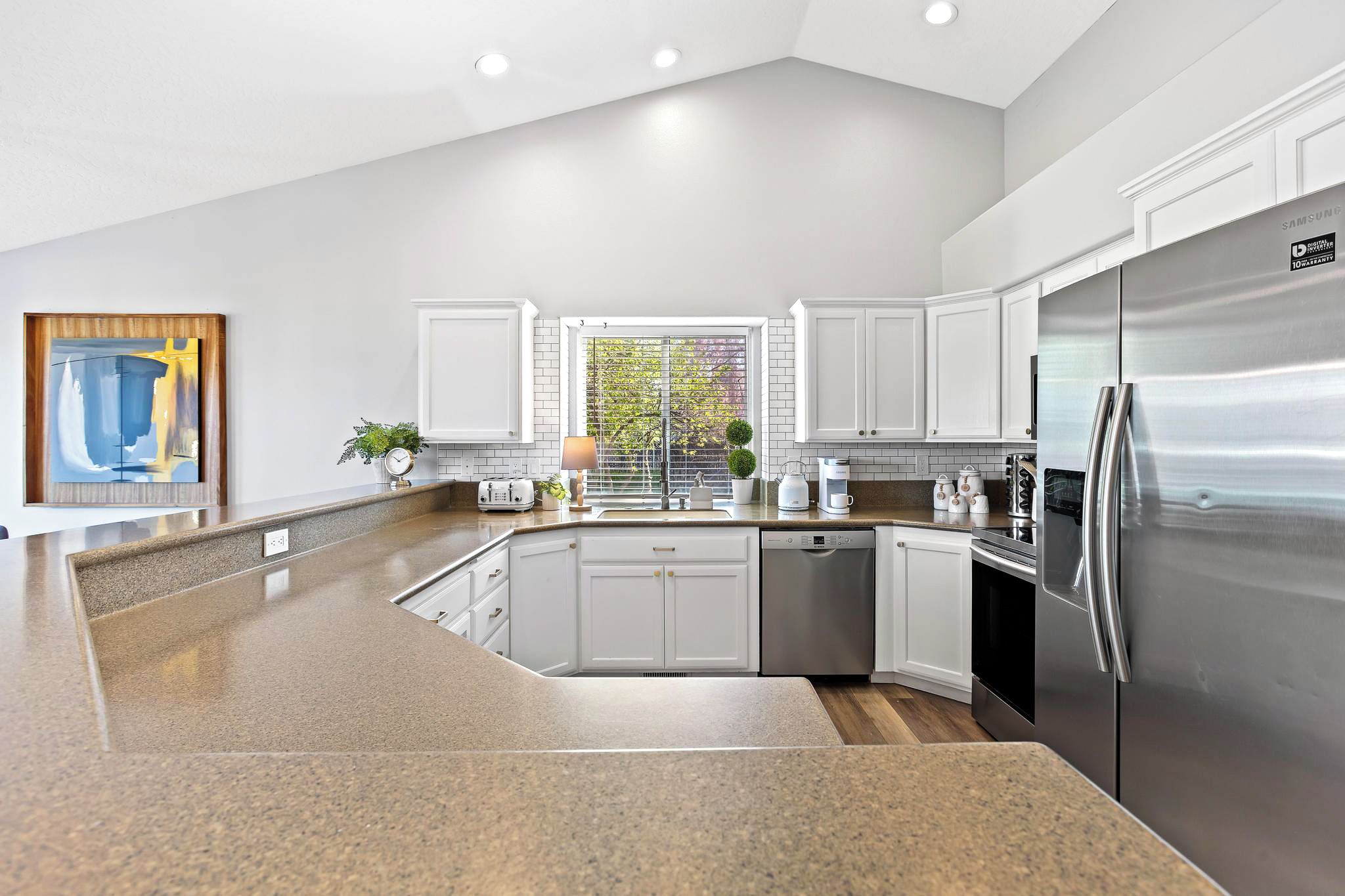 Una cocina moderna con armarios blancos, un refrigerador de acero inoxidable y una encimera de granito.