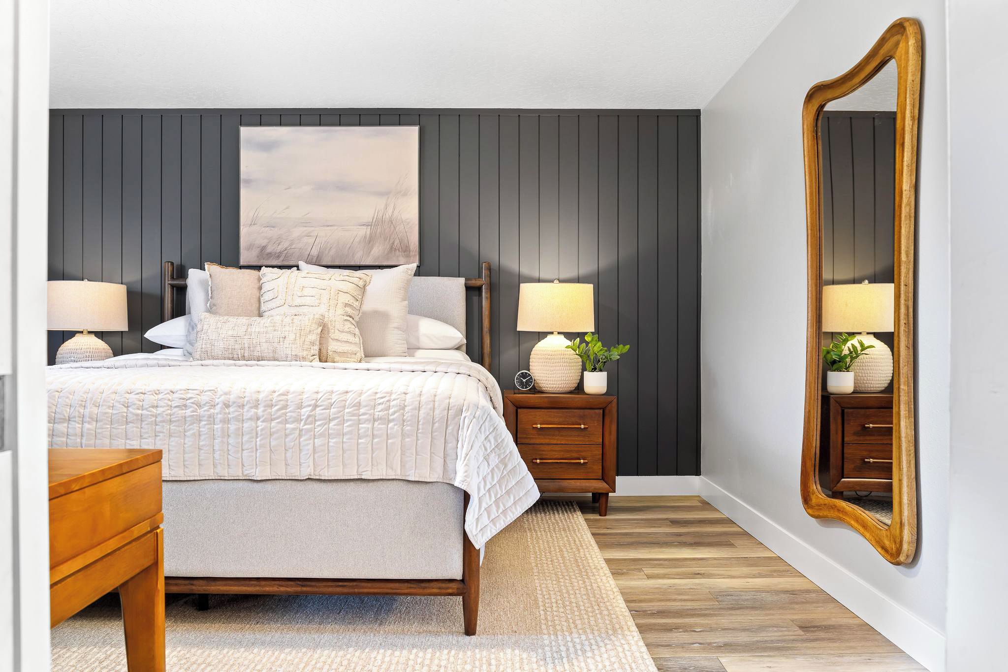 A bedroom with a bed, two nightstands, a mirror, and a large painting on the wall.