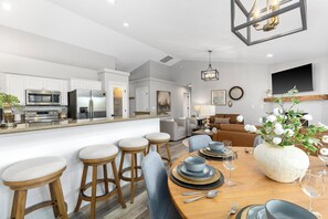 A modern kitchen with white cabinets, stainless steel appliances, and a dining area with a wooden table and bar stools. - Luxe Meridian Retreat •1K+3Q beds • 600+ WiFi • 3 Desks • Games • Prime Location (Meridian)