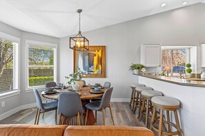 Eine moderne Küche mit Essbereich, Holzhocker und einem großen Fenster mit Jalousien.