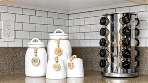 Three white kitchen jars with wooden labels for coffee, flour, and sugar, and a spice rack with black spice containers. - Luxe Meridian Retreat •1K+3Q beds • 600+ WiFi • 3 Desks • Games • Prime Location (Meridian)
