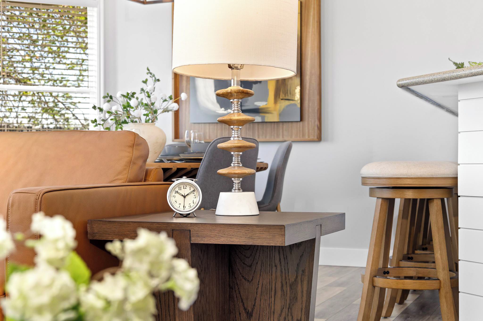 A modern living room with a wooden coffee table, a clock, a lamp, a sofa, and a stool.