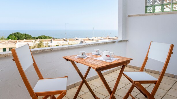 Un balcón con mesa y sillas, vista al mar y una ventana con diseño de cuadrícula.