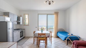 Cocina compacta con electrodomésticos modernos, comedor con mesa y sillas, una cama individual y un amplio ventanal con vistas.
