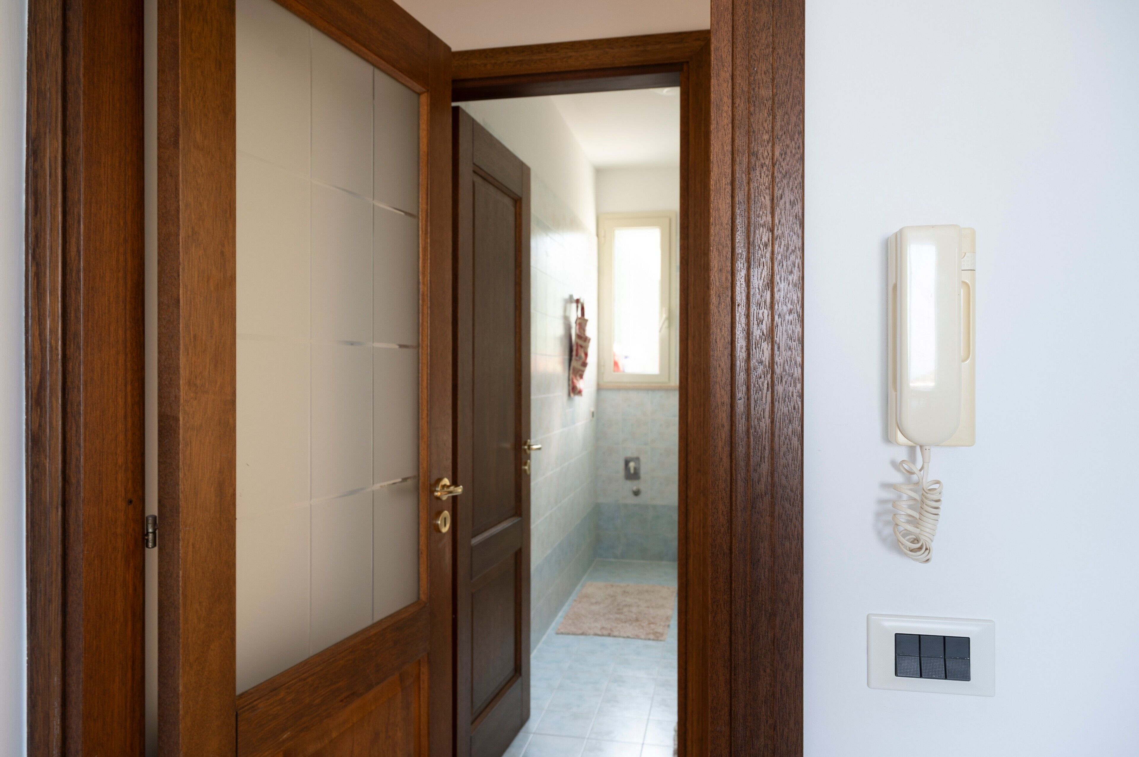A wooden door leading to a bathroom with a towel rack, a light switch, and a telephone.