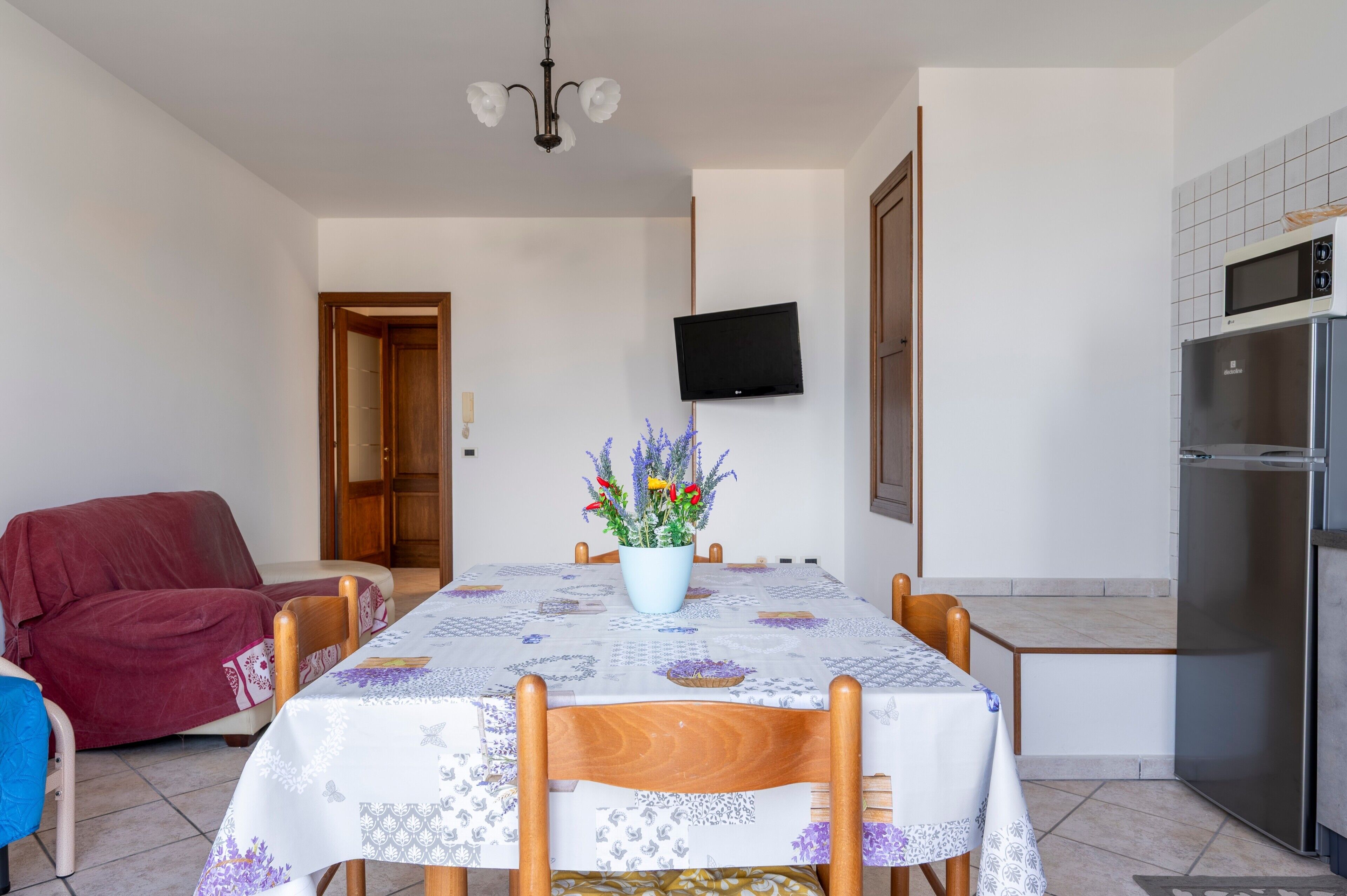 Un coin repas avec une table dressée pour quatre personnes, un téléviseur fixé au mur et un espace cuisine équipé d’un réfrigérateur.