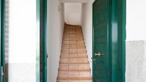 Una escalera conduce a una puerta verde, con paredes blancas y piso de baldosas.