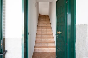 Un escalier menant à une porte verte, des murs blancs et un sol carrelé.