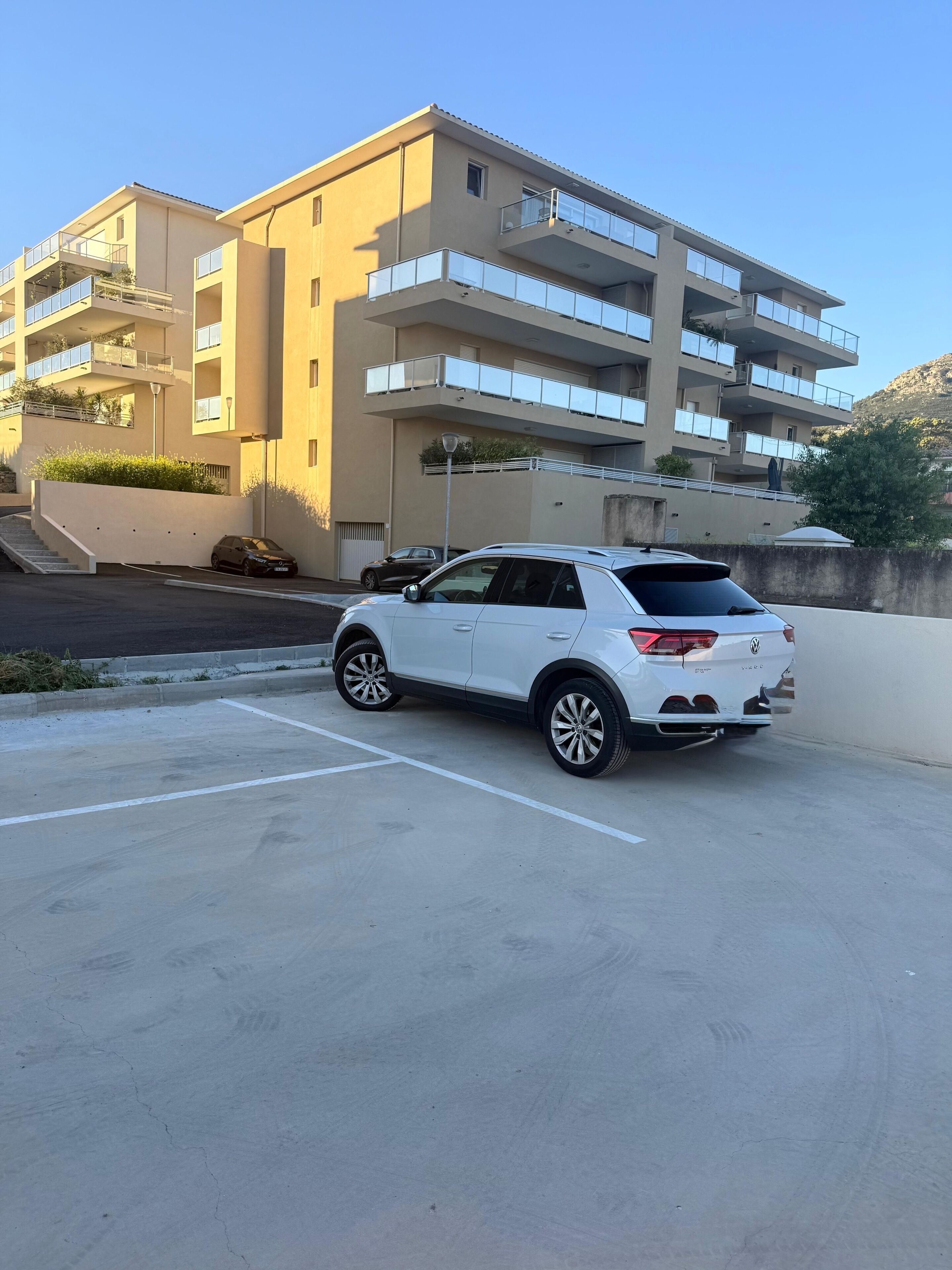Valkoinen maasturi on pysäköity parkkipaikalle, ja taustalla näkyy monikerroksinen rakennus.