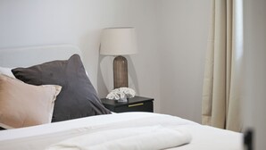 A neatly made bed with pillows, a bedside lamp, and a nightstand with a tissue box. - Modern 1BR Ground Floor Flat | City Centre Near High Street (Southend-on-Sea)