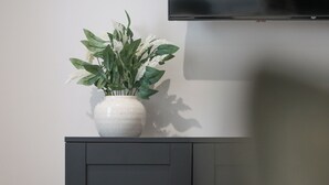 A white vase with green foliage on a dark cabinet against a plain wall. - Modern 1BR Ground Floor Flat | City Centre Near High Street (Southend-on-Sea)