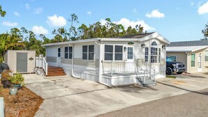 A mobile home with a front porch, a garage, and a small deck area. - Lakeside Lily Pad (Fort Myers)