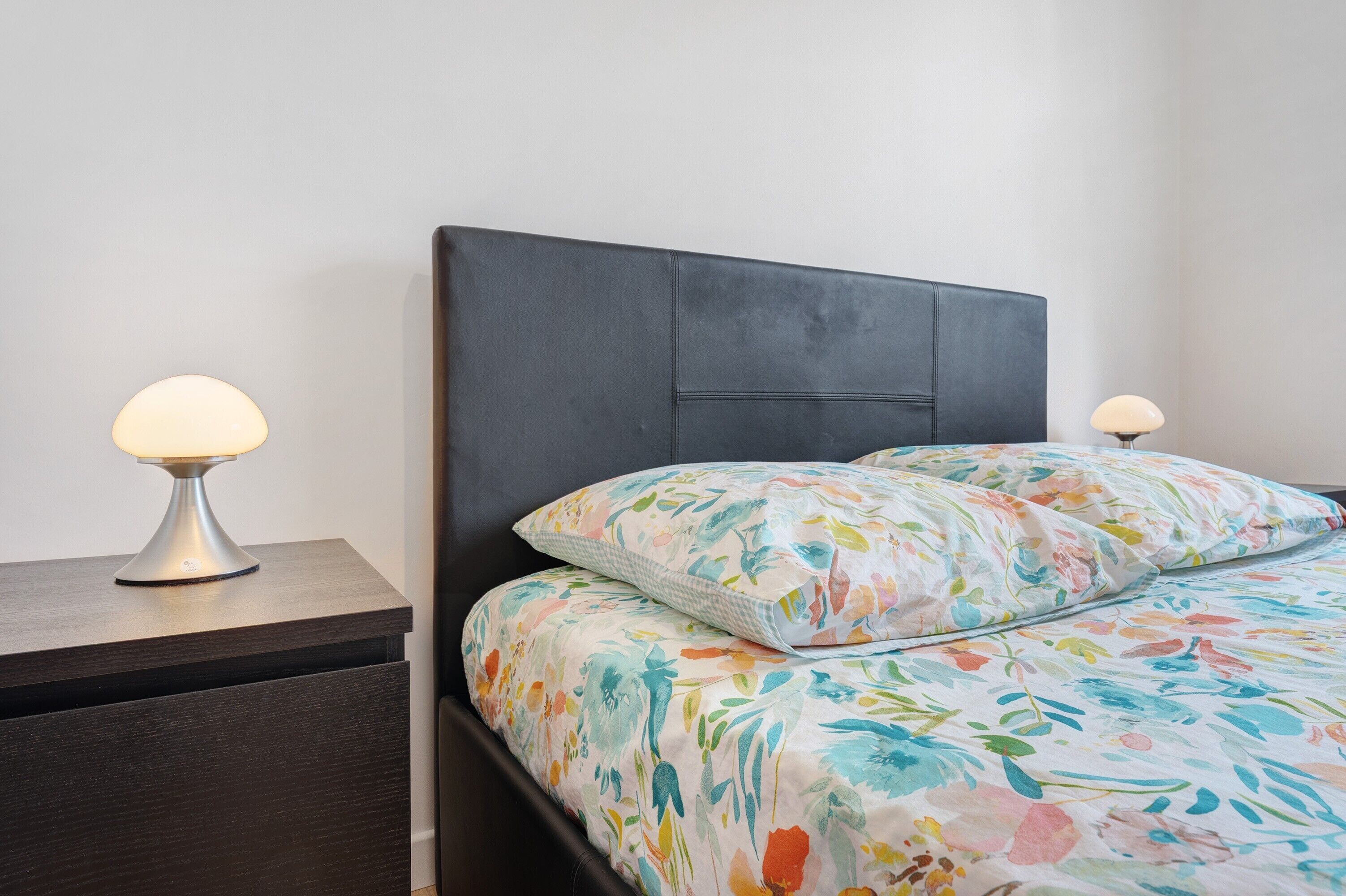 A bed with floral bedding, a dark headboard, and bedside lamps on a wooden nightstand.