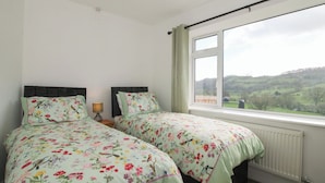A bedroom with two beds, a window with a view of hills, and a radiator. - Spring Bank (Llanfyllin)