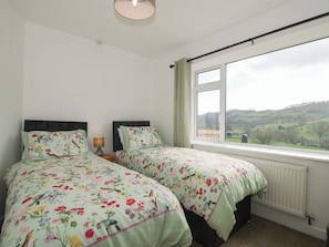 Un dormitorio con dos camas, una ventana con vistas a colinas y un radiador.