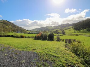 Paisaje rural con colinas onduladas, cielo despejado y una casa a lo lejos.