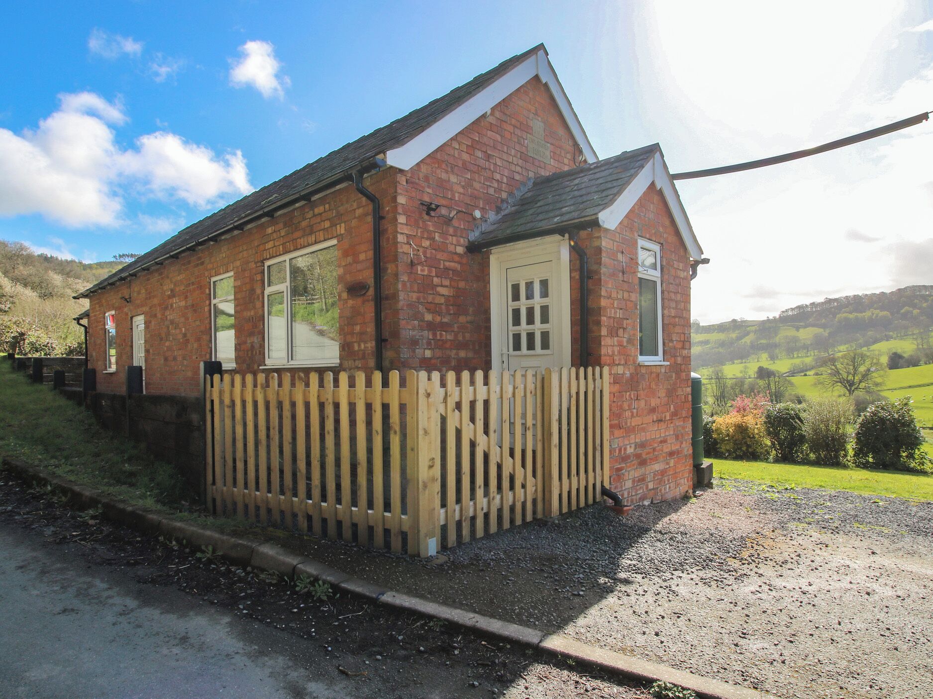 A small brick building with a wooden fence, a door, and windows.